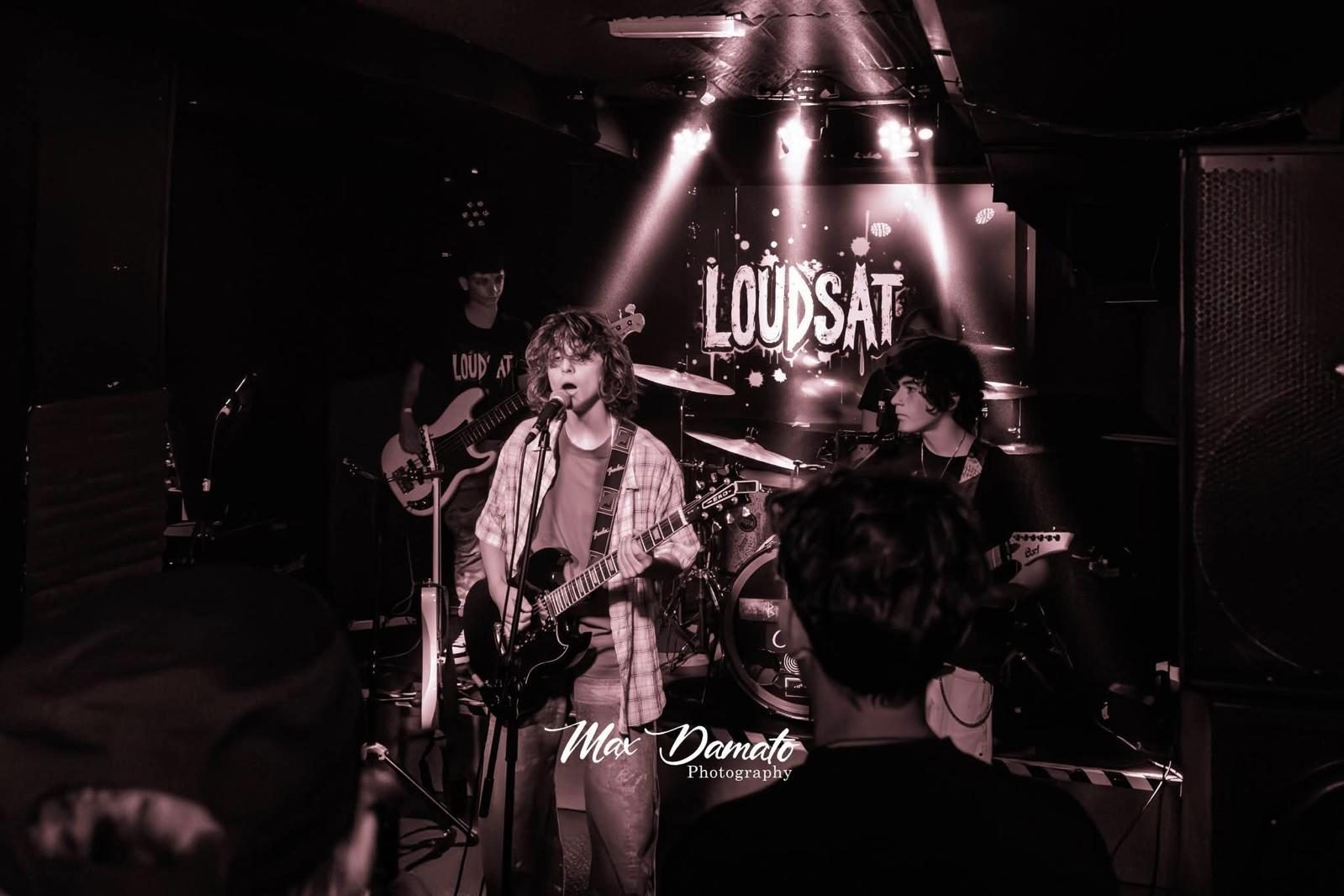 I Loudsat dal vivo sul palco, con il logo della band proiettato alle spalle